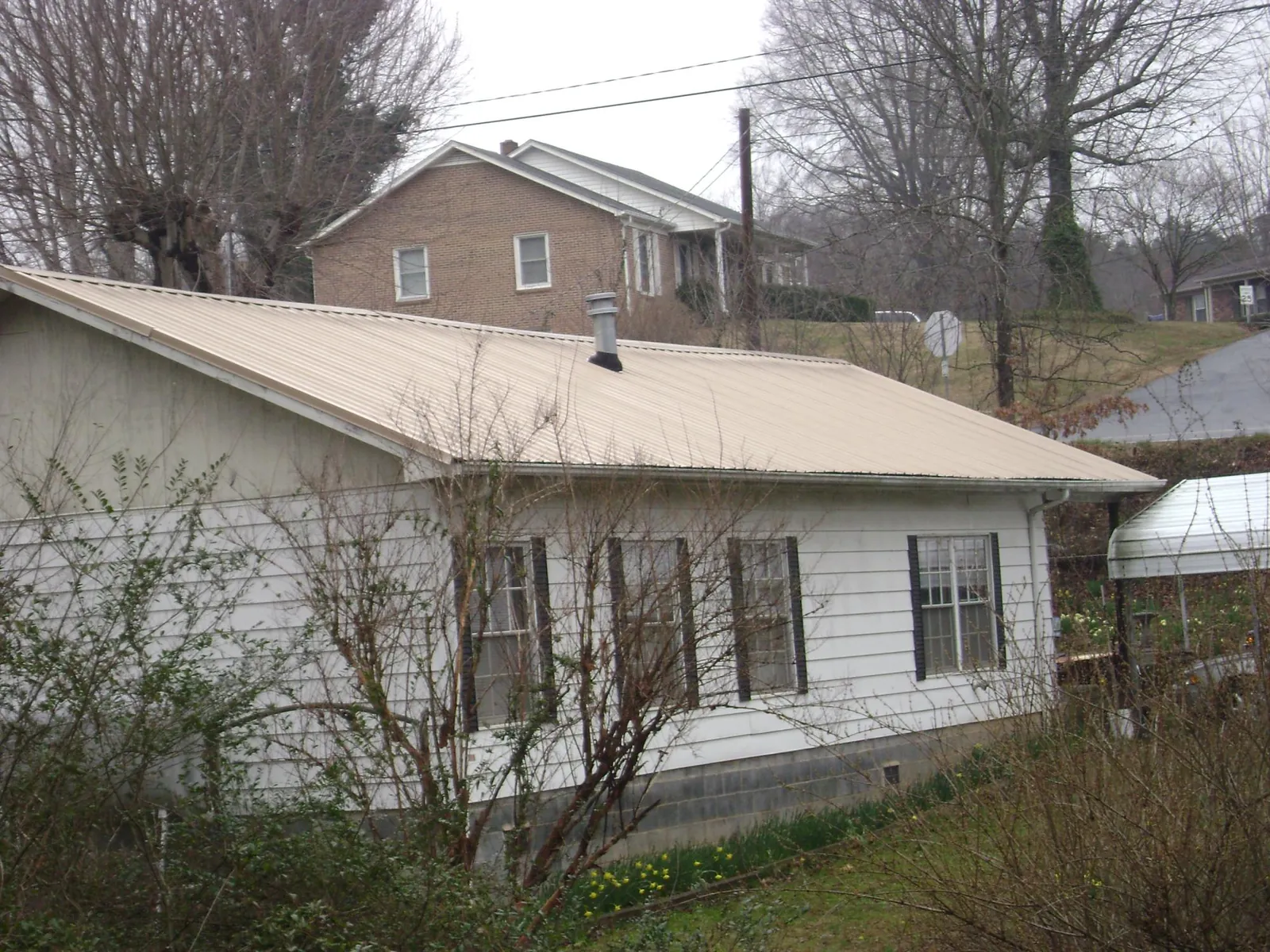 Tan metal roof on a white sided house set into a hillside — Commercial Roofing by Roofing Brothers in Miami